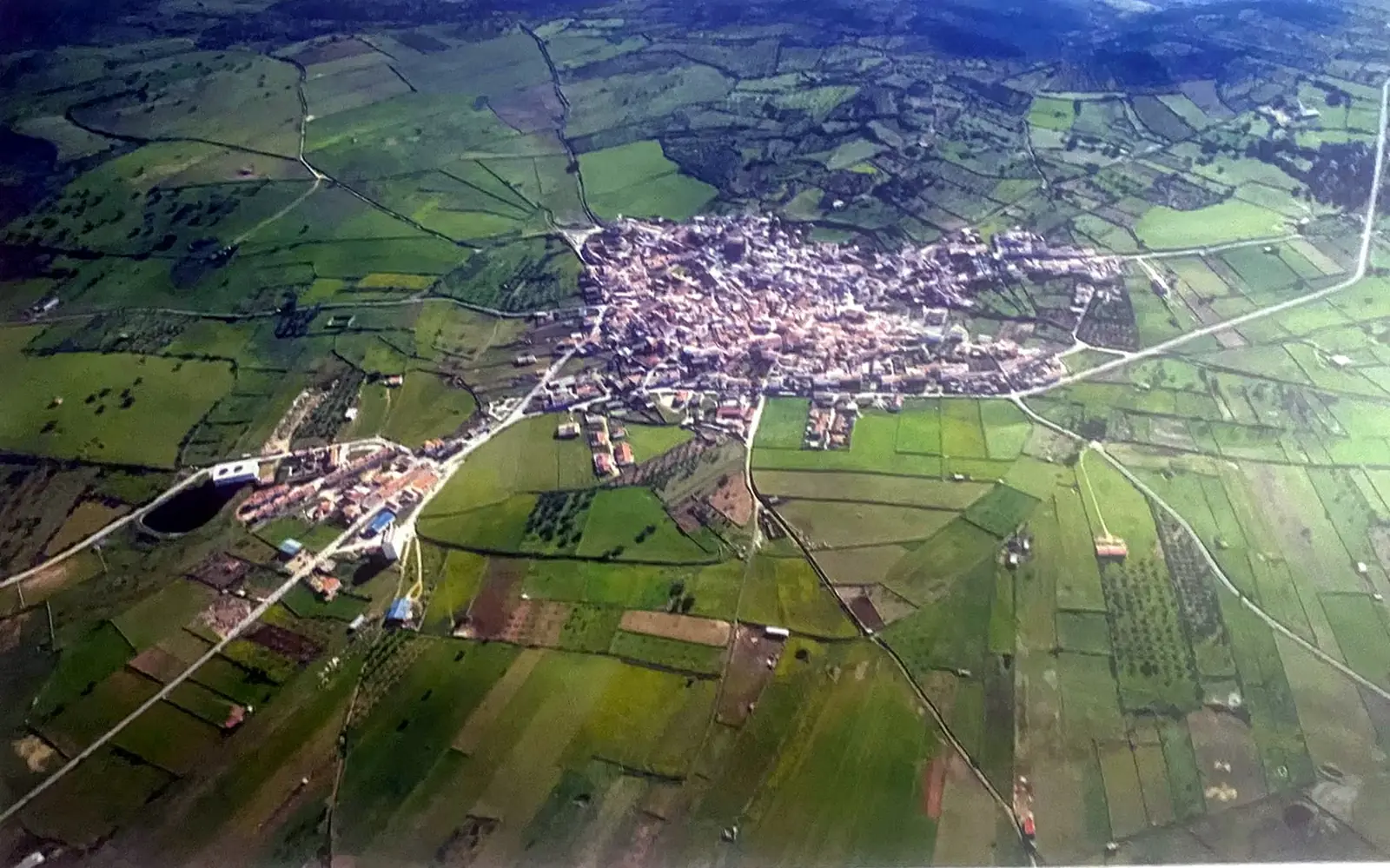 Vista aérea cenital del casco urbano de Ibahernando, compacto, del que parten caminos entre parcelas verdes.
