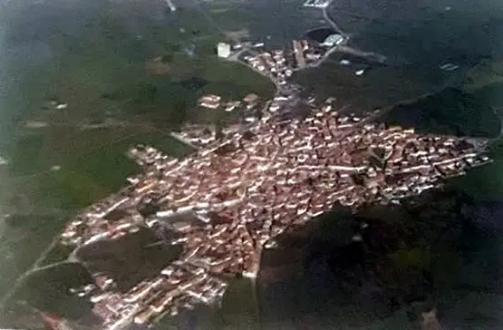 Vista aérea del pueblo alargado entre campos verdes, tomada desde el lado del Palomar.