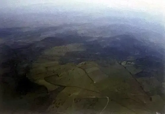 Paisaje aéreo de dehesa y lomas verdes que se pierden en la bruma del horizonte.