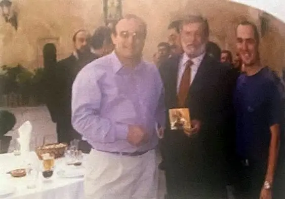 Tres hombres de pie en un salón; uno sostiene la carátula de un disco.