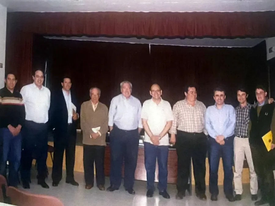 Una docena de hombres de pie en fila ante un telón de escenario.