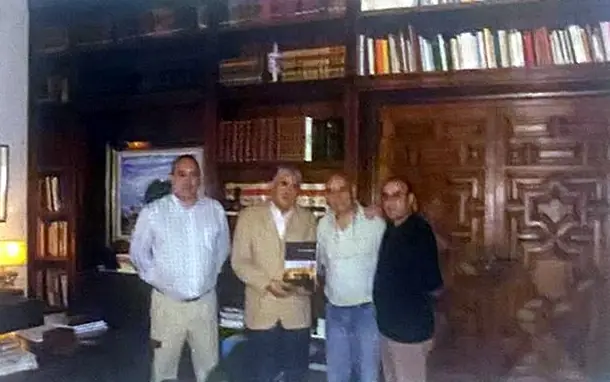 Cuatro hombres posan ante una estantería de libros en una sala con artesonado.
