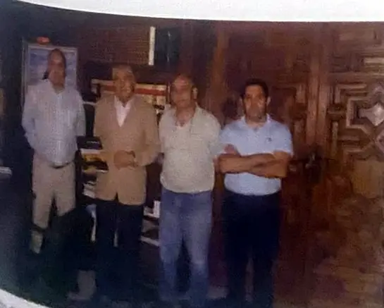 Cuatro hombres de pie en un despacho con puertas de madera tallada.