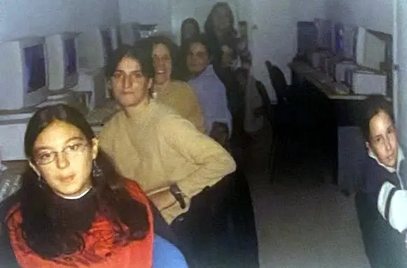 Grupo de jóvenes sonrientes junto a ordenadores en un aula pequeña.