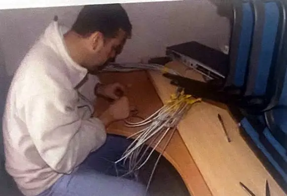 Un hombre inclinado sobre una mesa conecta un manojo de cables de red.